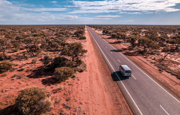 A Toyota Hiace campervan travelling along a long, straight outback highway in Western Australia.