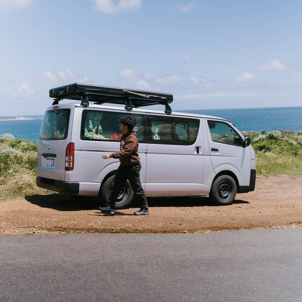 Man walking in front of booked 2-5 seater campervan overlooking coast