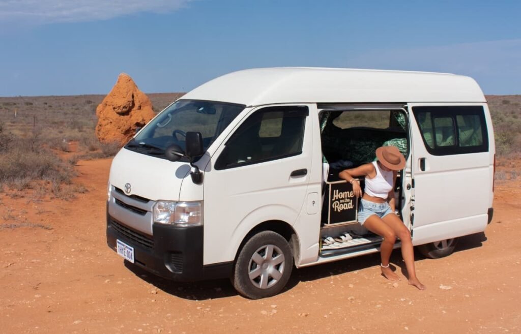 Traveller stepping out of a high top Toyota Hiace campervan parked in the Western Australian outback.