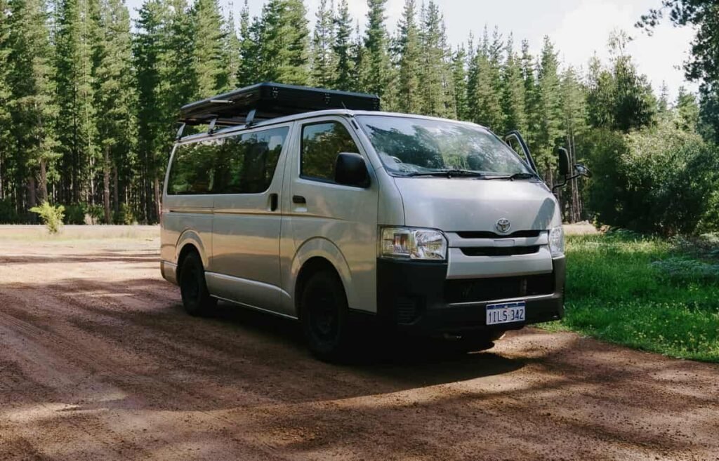 2–5 seater Toyota Hiace campervan parked on a forest road surrounded by tall trees.