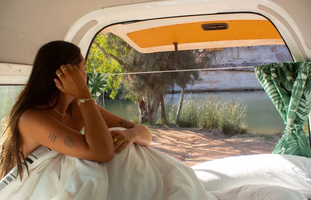 woman in back of campervan looking out while on summer road trip in wa