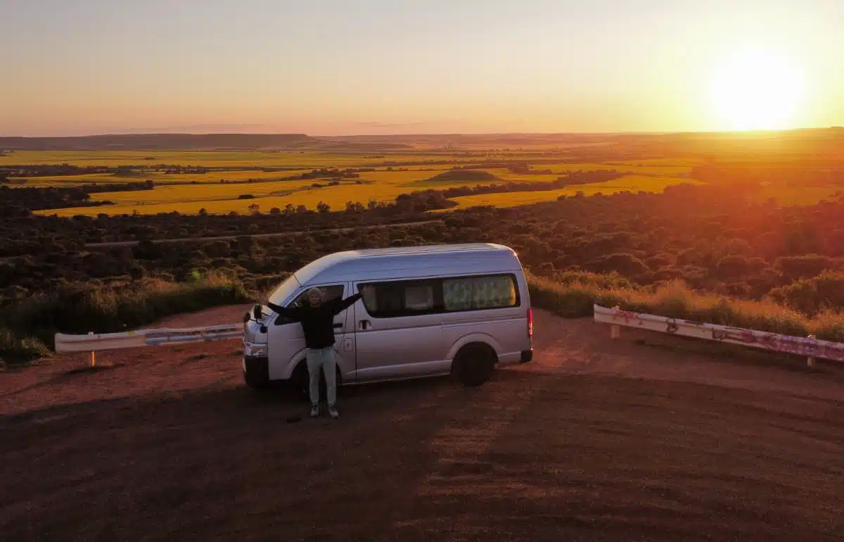 Person standing in front of campervan as sun sets over field