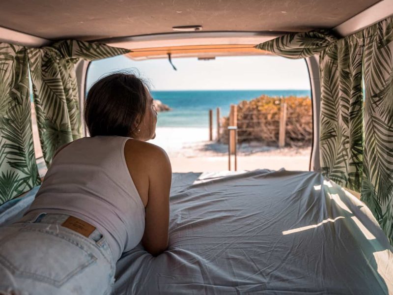 Woman laying in van looking out open back door over one of the best WA beaches for summer roadtrip